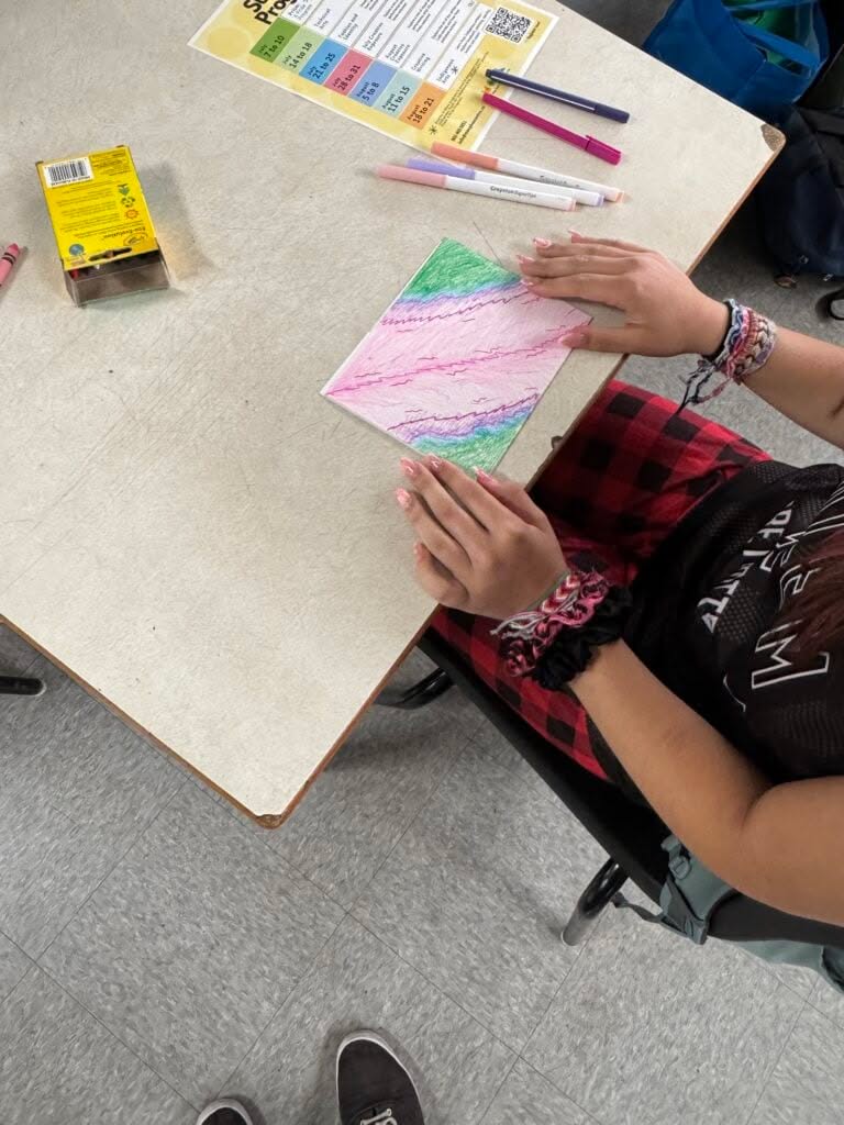 An over the shoulder picture of an individual working on a colourful drawing at a grey table