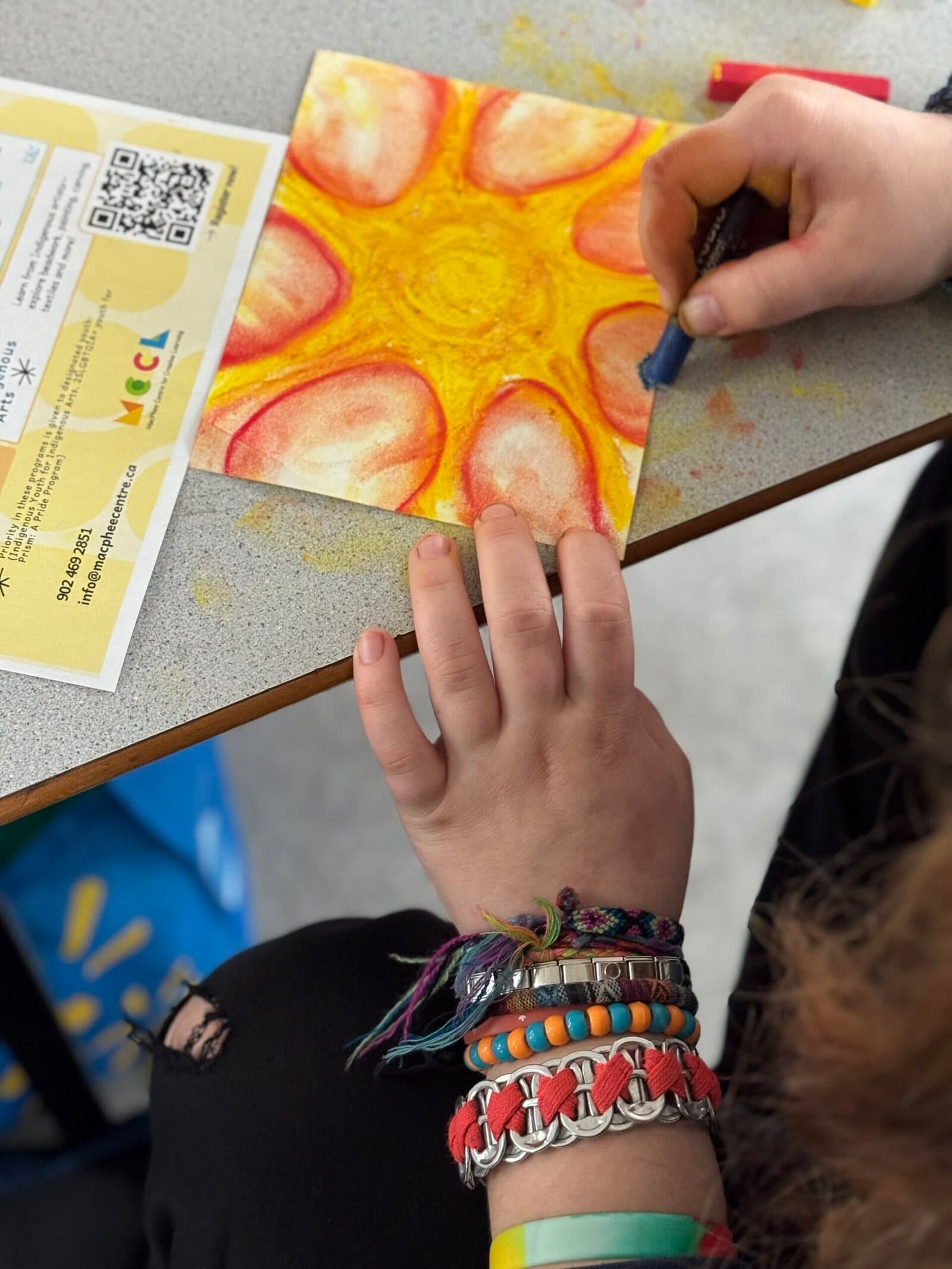 Two hands use warm tone pastels to create abstract drawing.